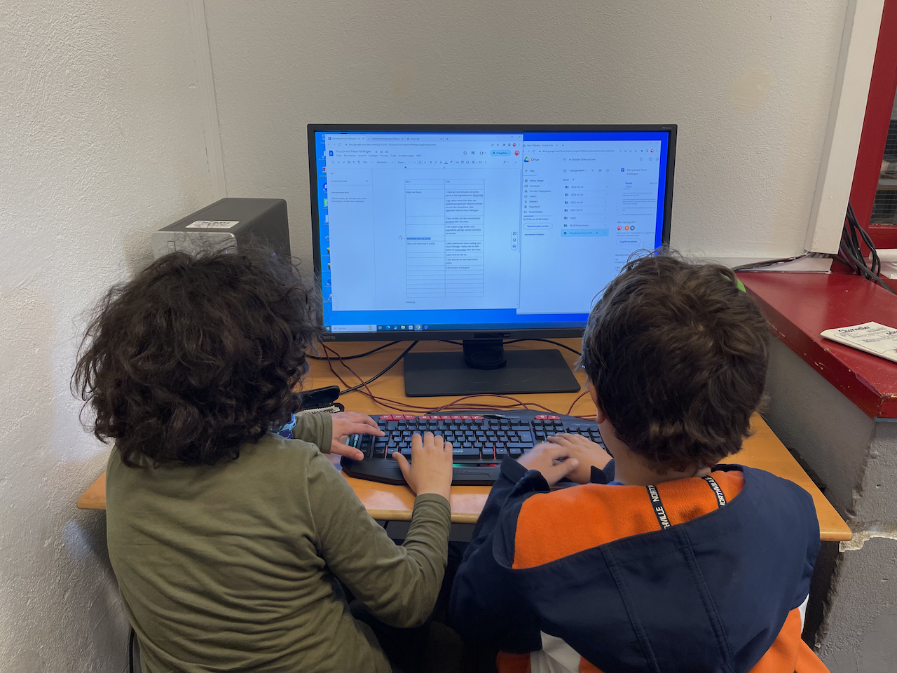zwei Jugendliche sitzen vor einem Computer an einem Schreibtisch