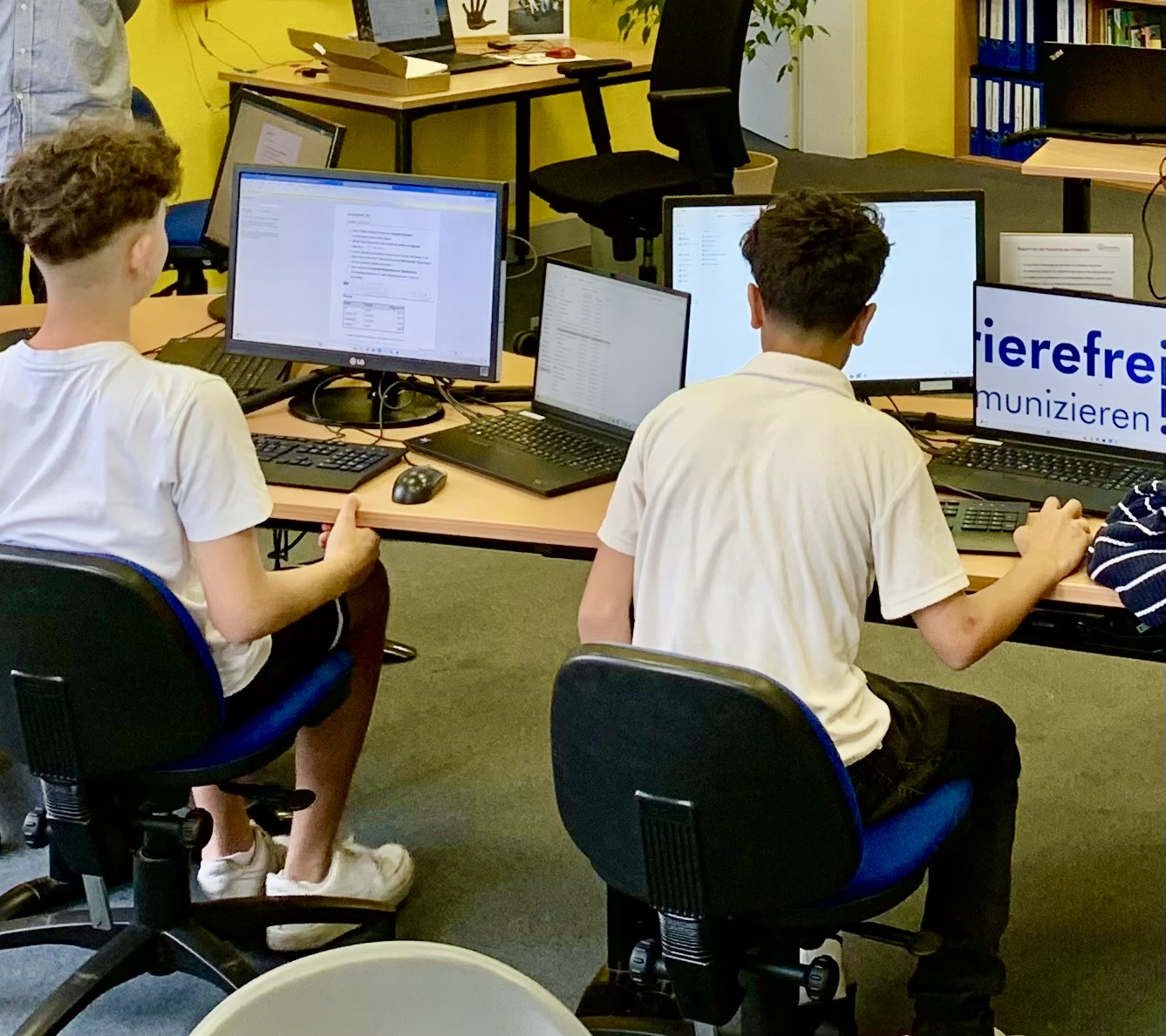 Projektfoto von barrierefrei kommunizieren! Bonn: Zwei Jugendliche sitzen an einem Schreibtisch und arbeiten an Computern und Laptops