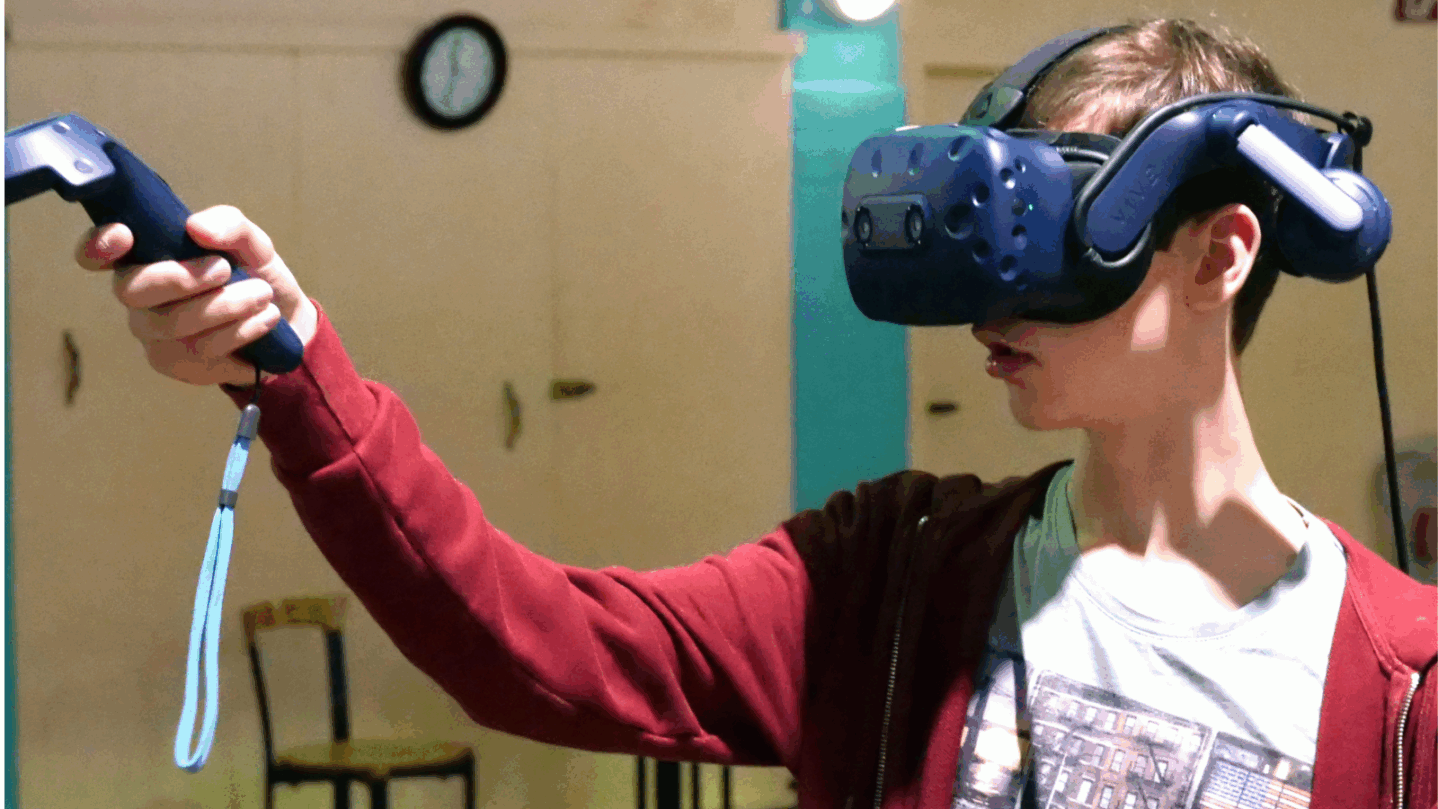 Ein Jugendlicher trägt eine VR-Brille und hält einen Controller in seiner Hand.