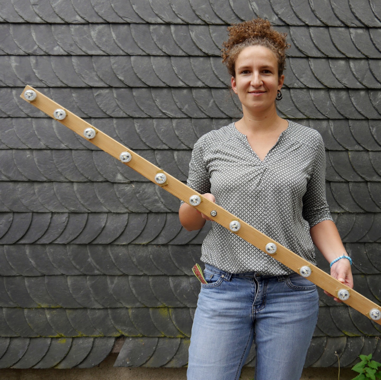 Eine Fachkraft hält eine selbstgebaute Lichtquelle in den Händen: ein großer Holzstab, an dem LED-Lichter angebracht sind.