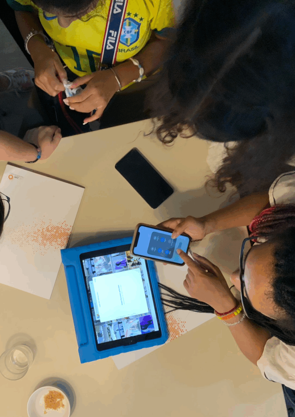 Bild von oben aufgenommen: Jugendliche sitzen um einen Tisch und arbeiten mit Tablets, Smartphones und Stift und Block, um Ideen zu sammeln