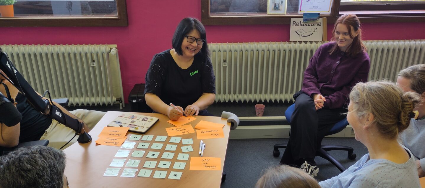 Fachkräfte sitzen in einer Stuhlgruppe und lachen, während sie auf Zetteln Notizen machen.
