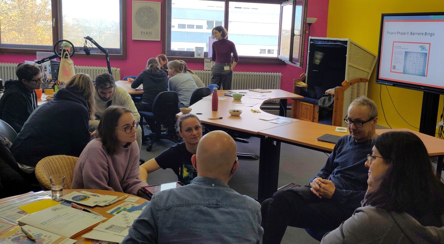 Blick durch den Raum. Die Fachkräfte sitzen in verschiedenen Kleingruppen zusammen und tauschen sich aus.