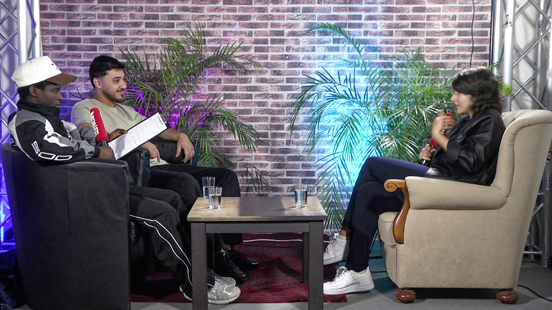 Jugendliche im TV-Studio von Kanal21, die ein Interview mit einem Gast führen. Alle sitzen auf Sesseln.