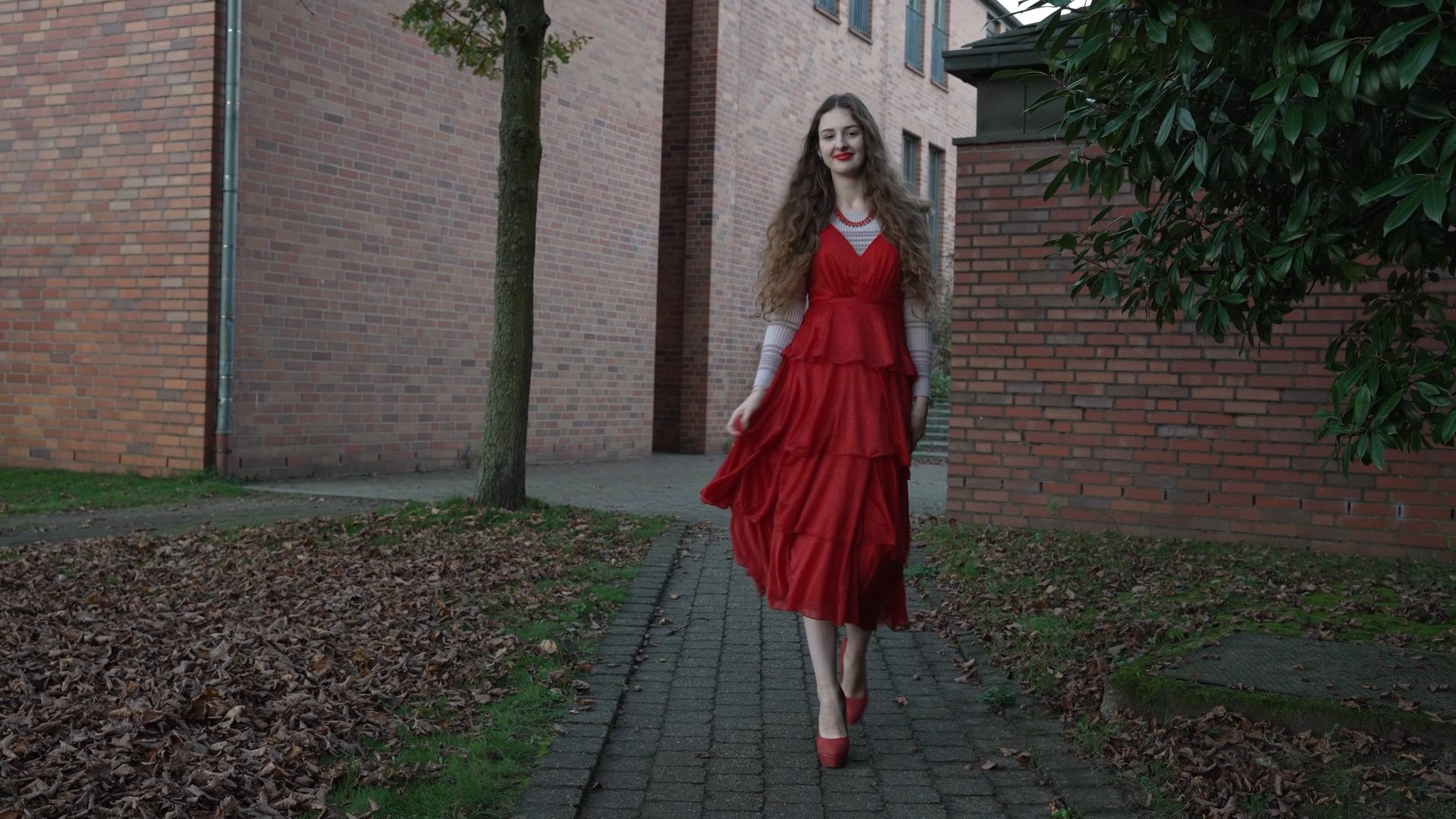 Eine Jugendliche in einem roten Kleid. Sie läuft auf die Kamera zu.
